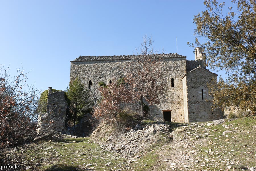 st-donat-02web.jpg - Saint Donat le Bas - Façade Sud. Celle-ci présente 5 ouvertures sans ornements, très ébrasées vers l'intérieur. Cette façade comme la façade nord est depourvue de contreforts. Les façades sont parsemées de trous de boulins qui servaient à l'ancrage des échaffaudages de bois. La façade Nord ne comporte aucune ouverture hormis une porte donnant sur le devant du coeur