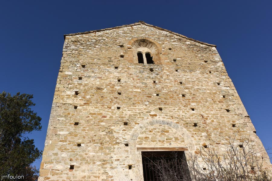 st-donat-27web.jpg - Saint Donat le Bas - Façade occidentale. Elle offre une large porte dont l'arc en plein cintre soulage le linteau. En haut au centre, se trouve une baie géminée insérée dans un plein cintre fortement ébrasé et admirablement appareillé. Celle-ci est également parsemée de nombreux trous de boulins